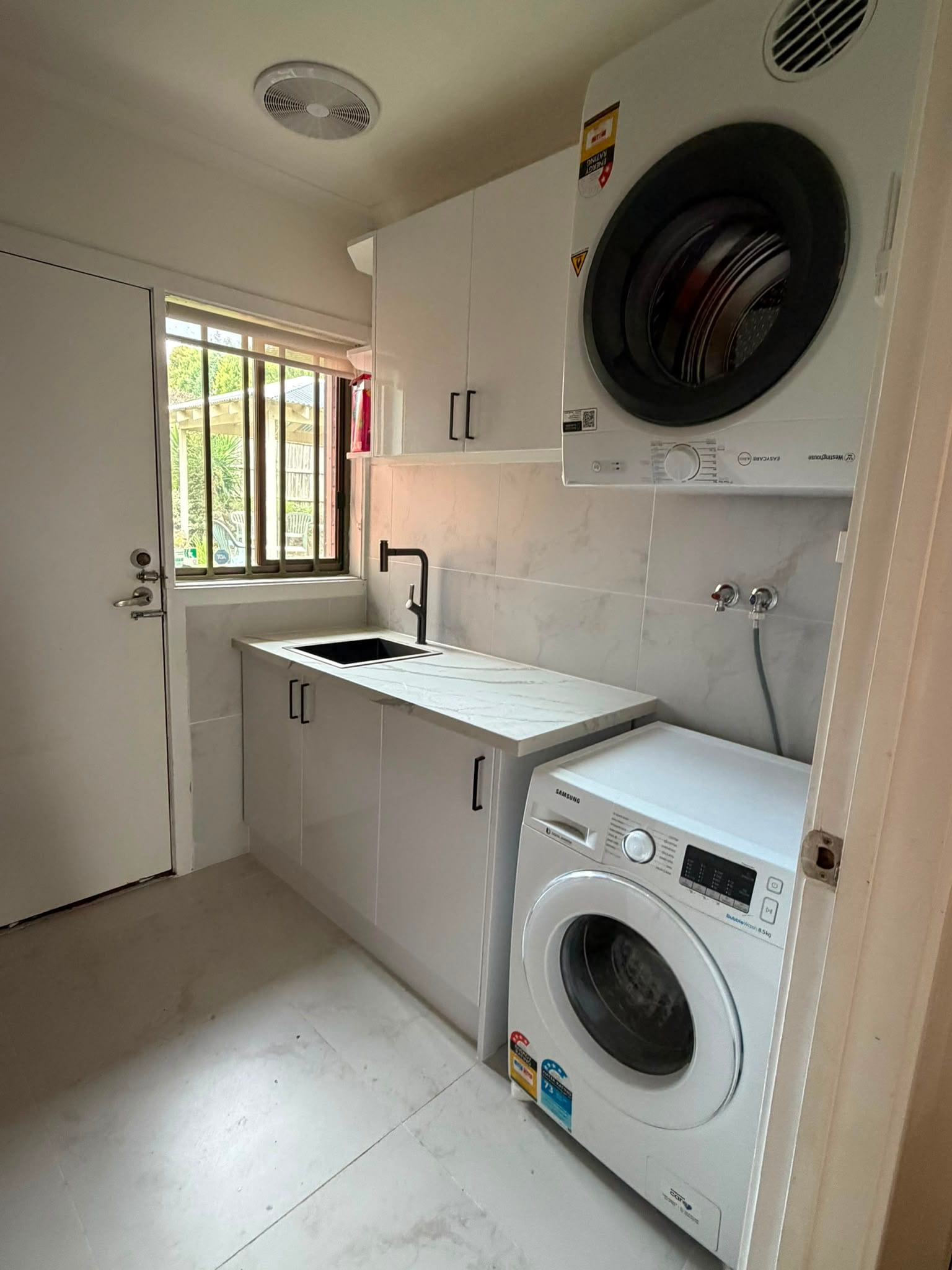 Renovated Melbourne laundry with stone bench and stacked washer and dryer